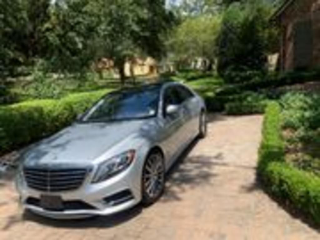 A silver mercedes benz is parked in a driveway next to a house.