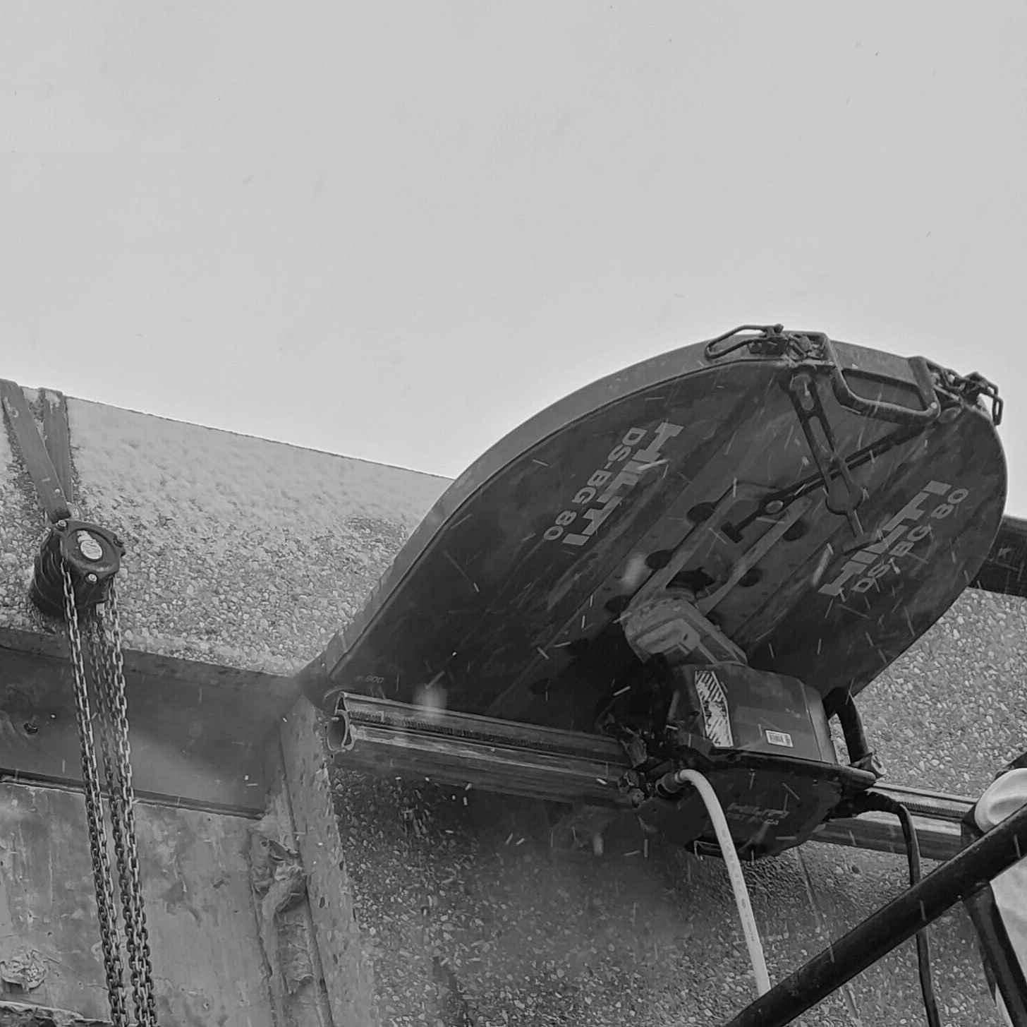 A black and white photo of a machine cutting a concrete wall.
