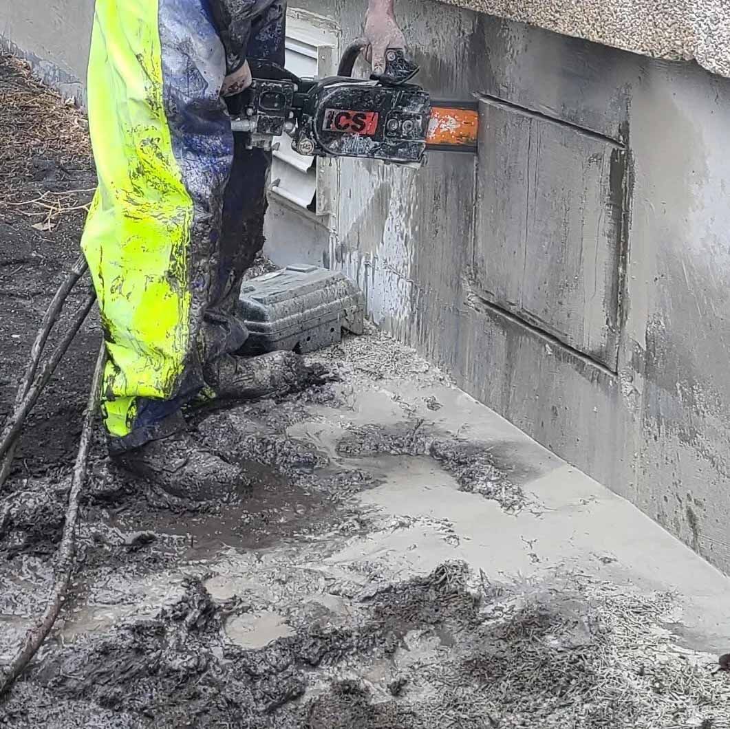 A man is cutting a hole in a wall with a chainsaw.