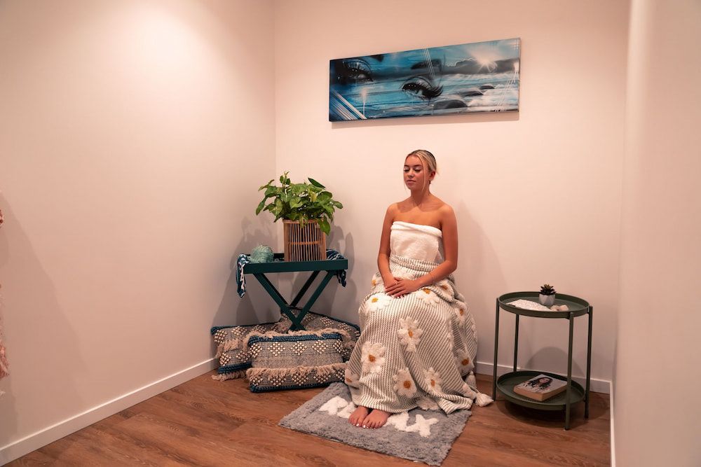 A Woman Wrapped in a Towel is Sitting on a Rug in a Room — Yoni Steam Australia in Gold Coast, QLD