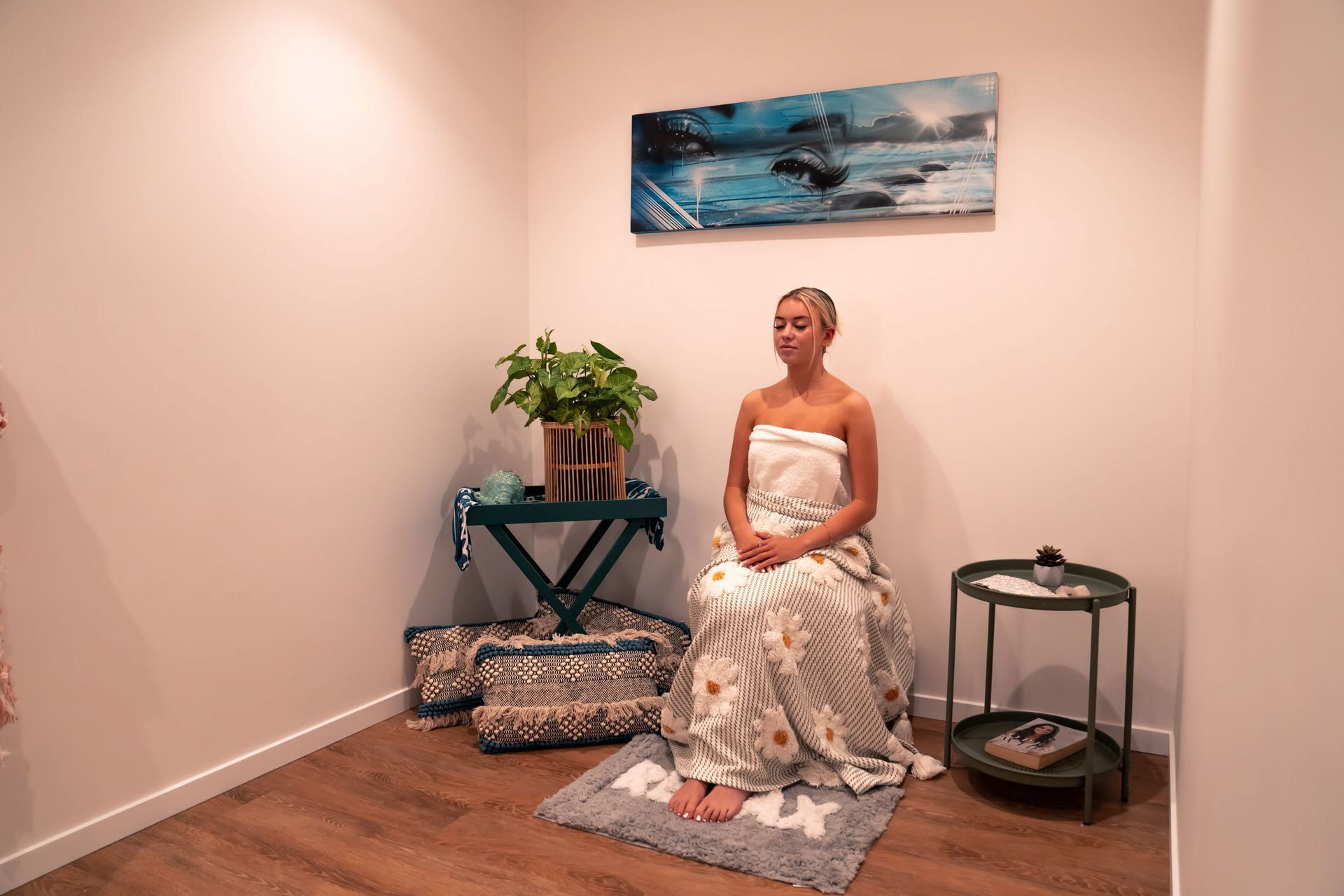 Woman meditating in a serene room, draped in white cloth, beside a plant and small table — Yoni Steam Australia in Gold Coast, QLD
