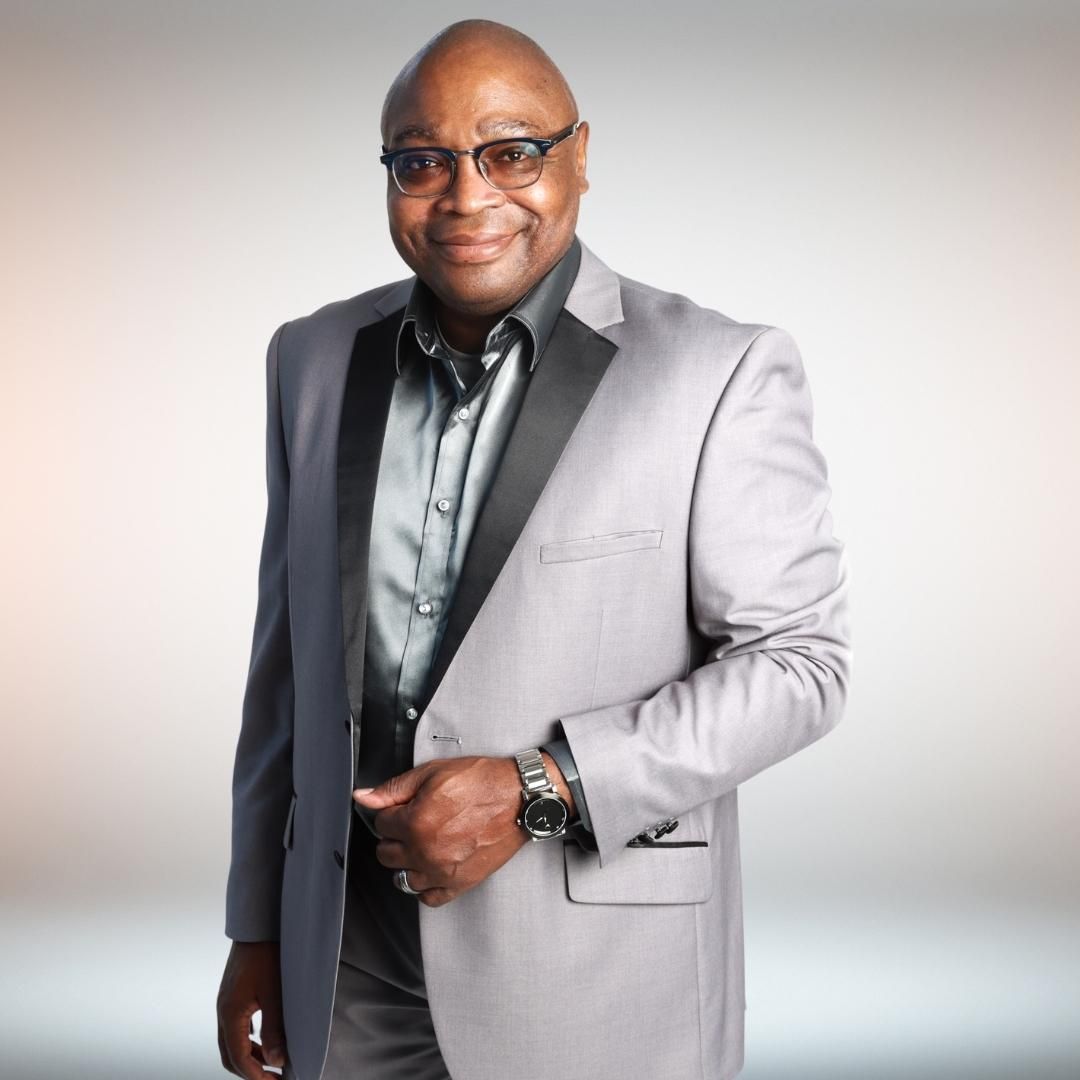 A man wearing a suit and glasses is smiling for the camera