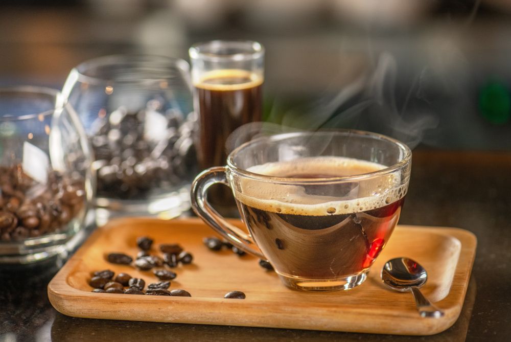 A Cup Of Coffee Is Sitting On A Wooden Tray Next To Coffee Beans — Casa Portugal In South Hurstville, NSW