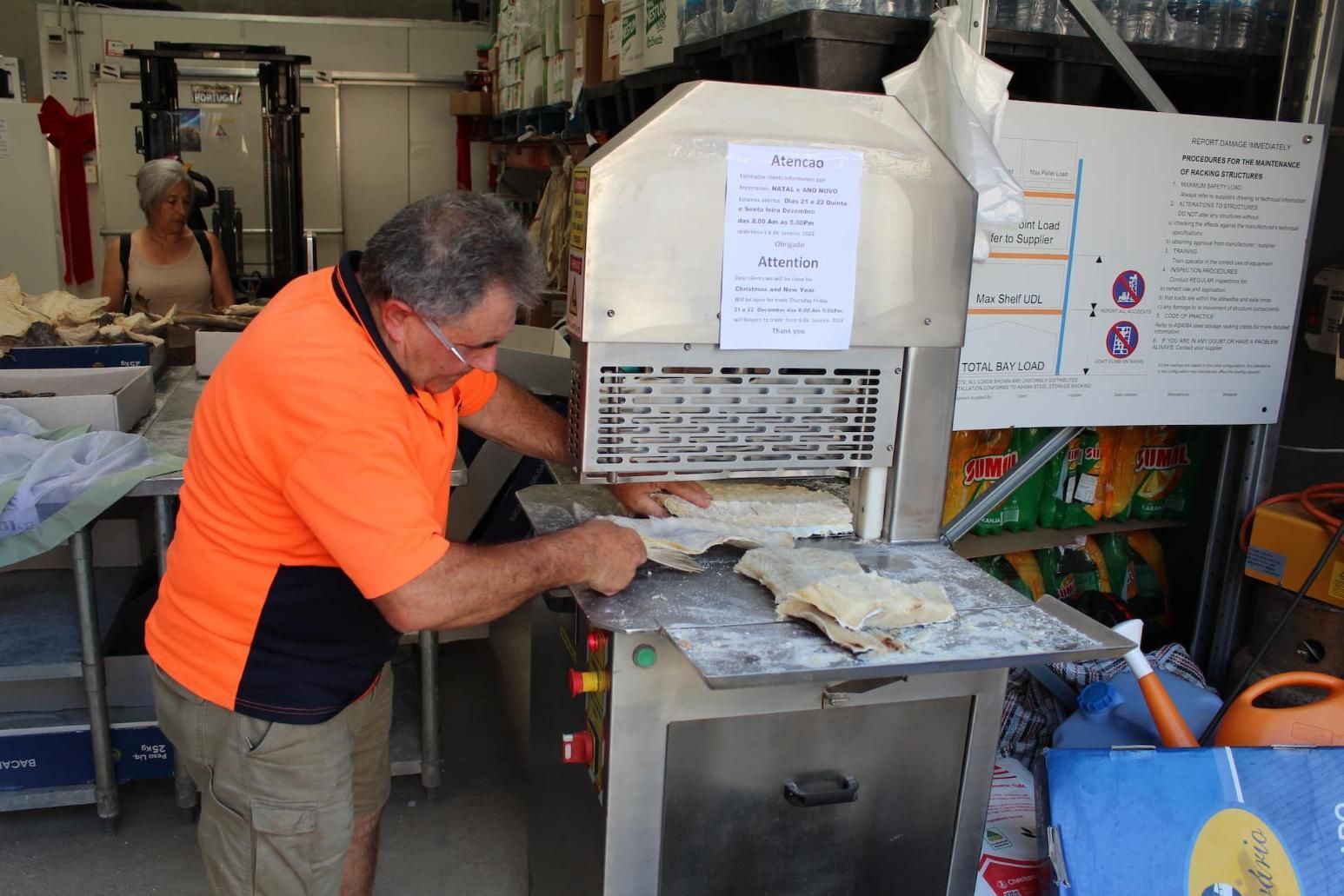 A Man In An Orange Shirt Is Working On A Machine In A Kitchen — Casa Portugal In South Hurstville, NSW