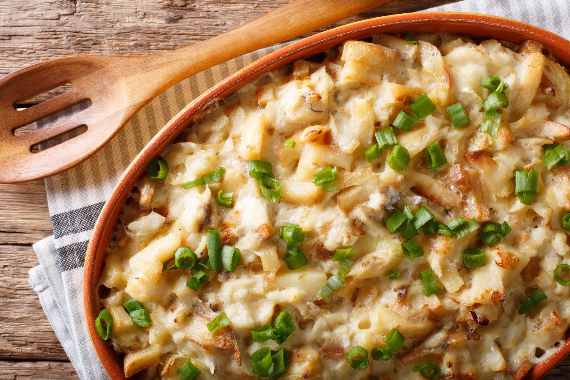 A bowl of macaroni and cheese with green onions and a wooden spoon on a wooden table — Casa Portugal In South Hurstville, NSW