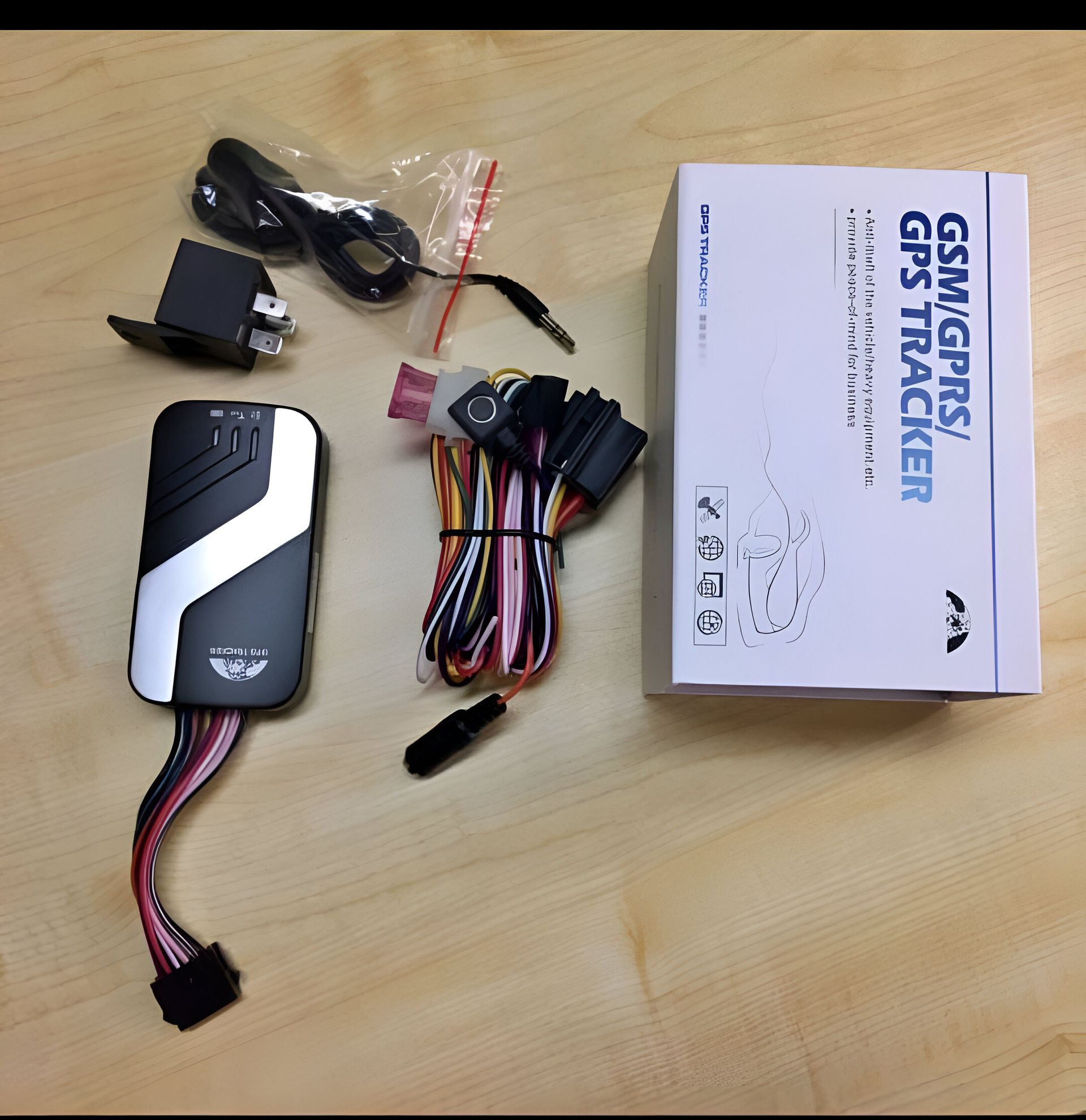 Kit rastreador GPS con cables, caja y componentes sobre superficie de madera.