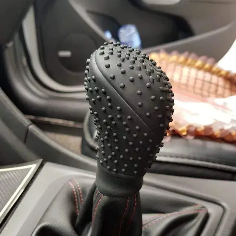 Pomo de palanca de cambios negro con pequeñas protuberancias y costuras rojas alrededor de la base. Interior de coche.