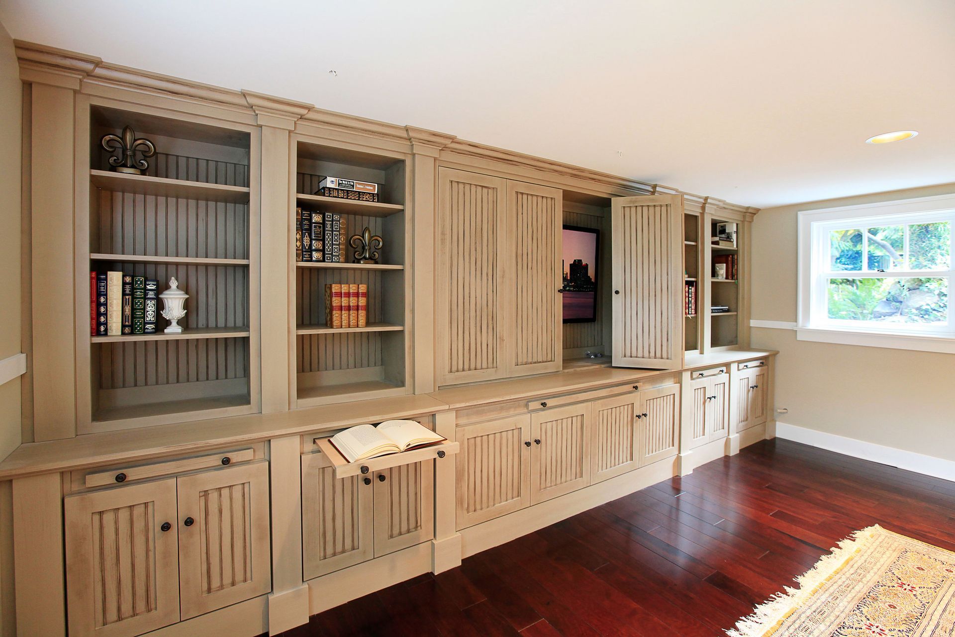Built-in wooden wall cabinets and storage in a bright room with hardwood floors and a window
