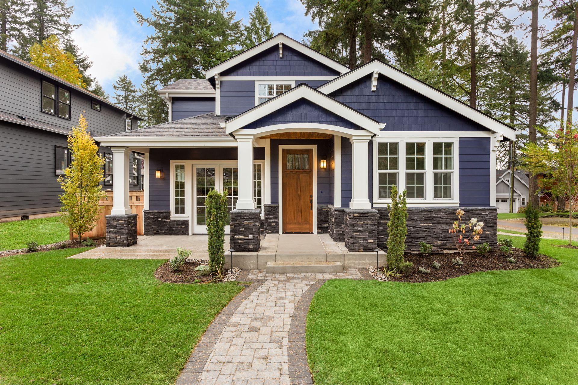 Blue cottage-style house with a front porch, stone steps, and a curved walkway surrounded by green lawn.