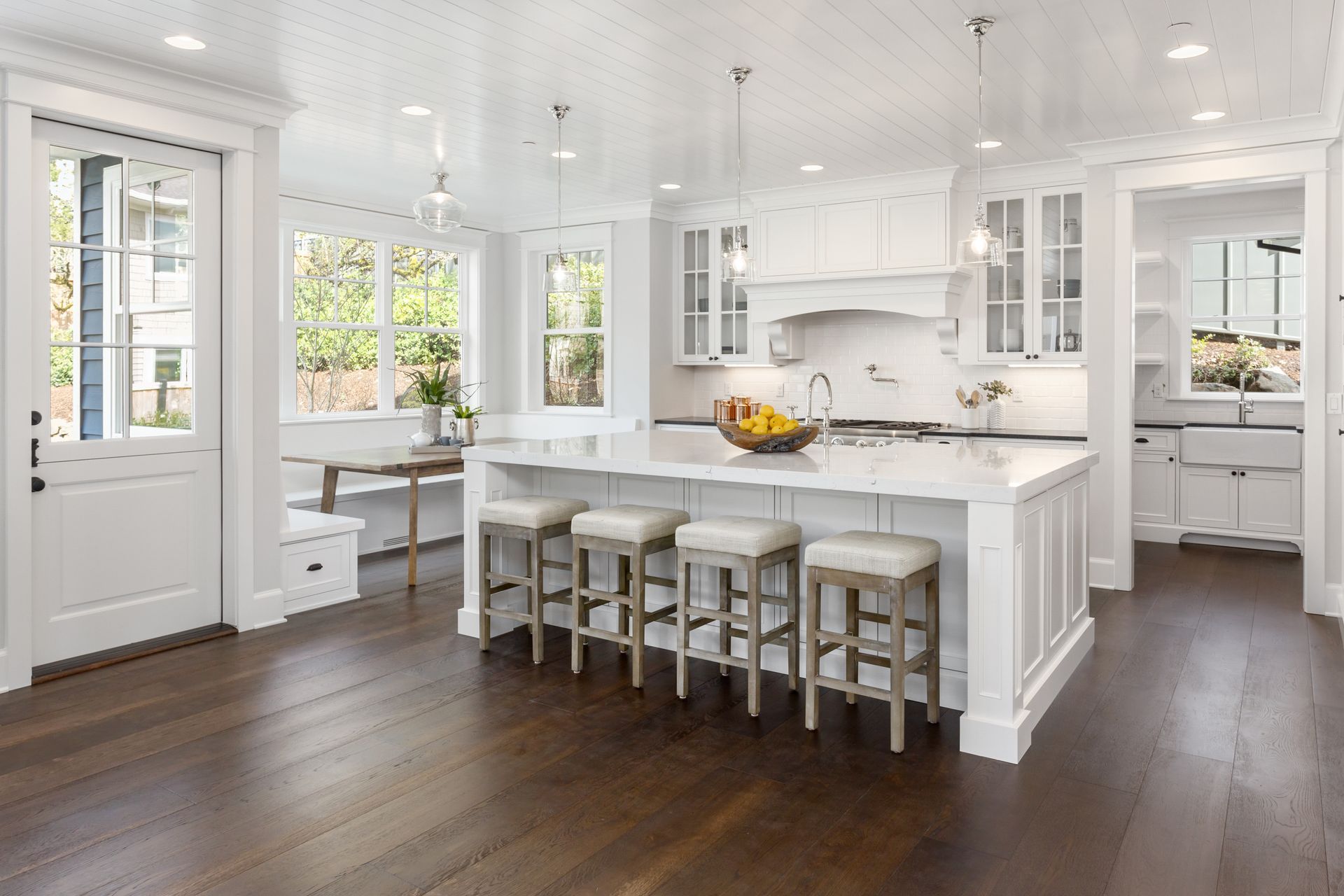 Bright white modern kitchen with island, bar stools, dark wood floors, and large windows
