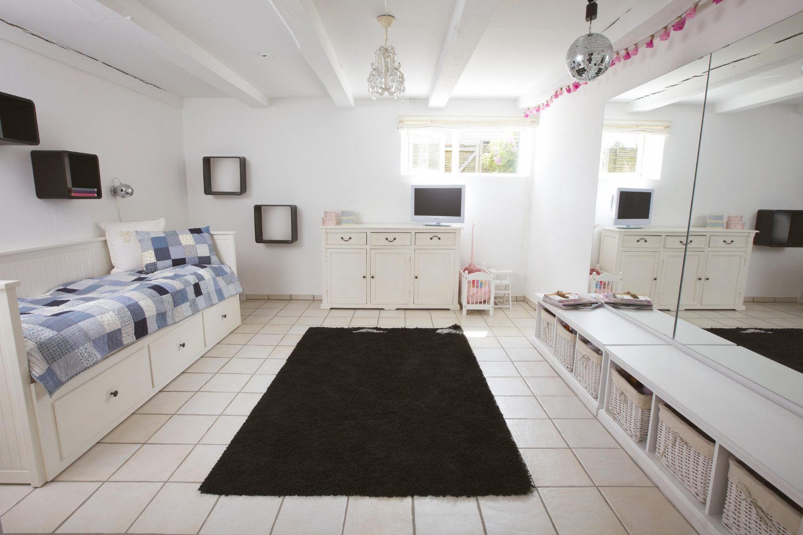 Bright white living room with tiled floor, black rug, white cabinets, blue sofa, and low benches
