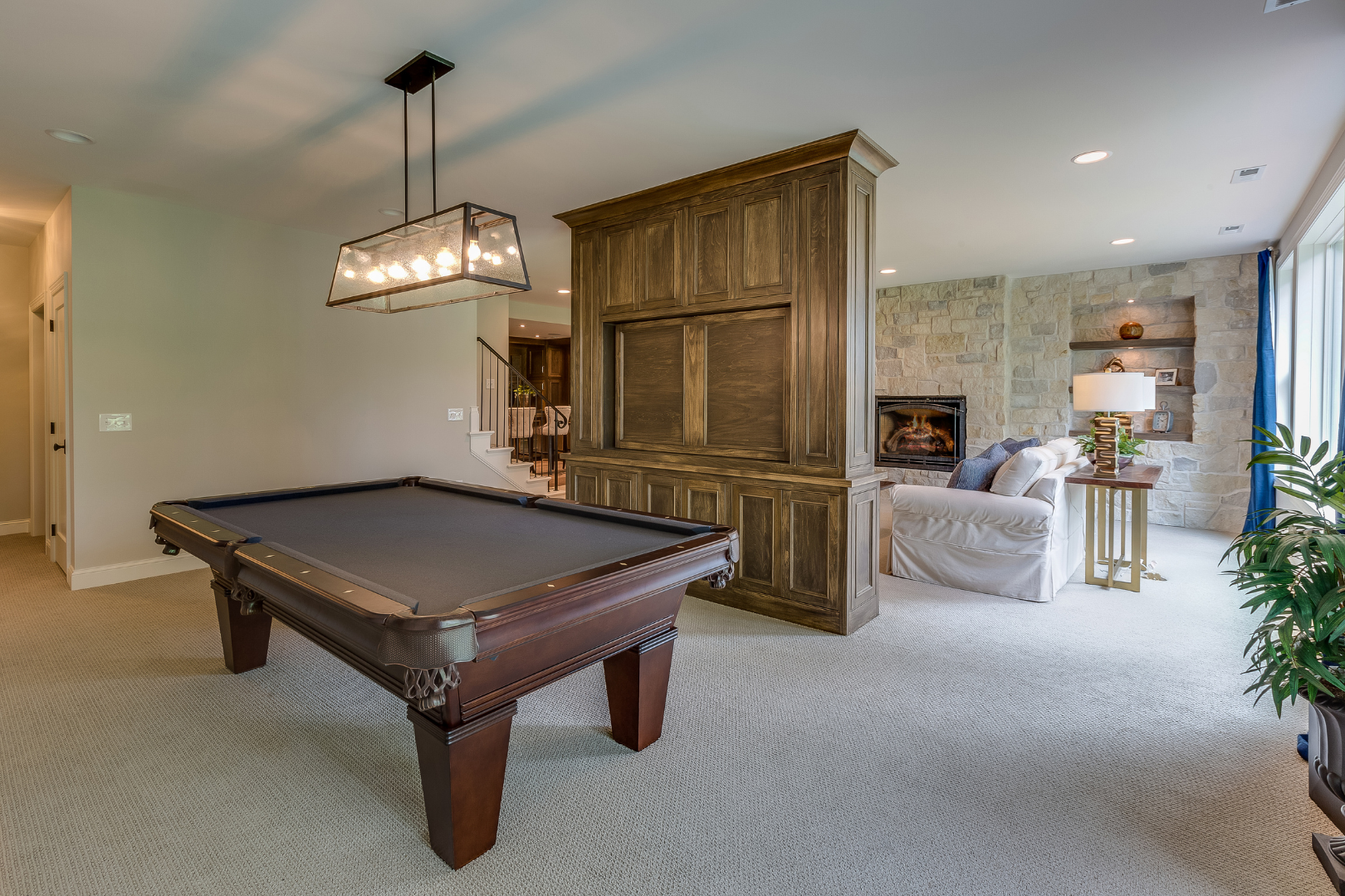 Spacious game room with a pool table, sectional sofa, fireplace, and wood-paneled divider