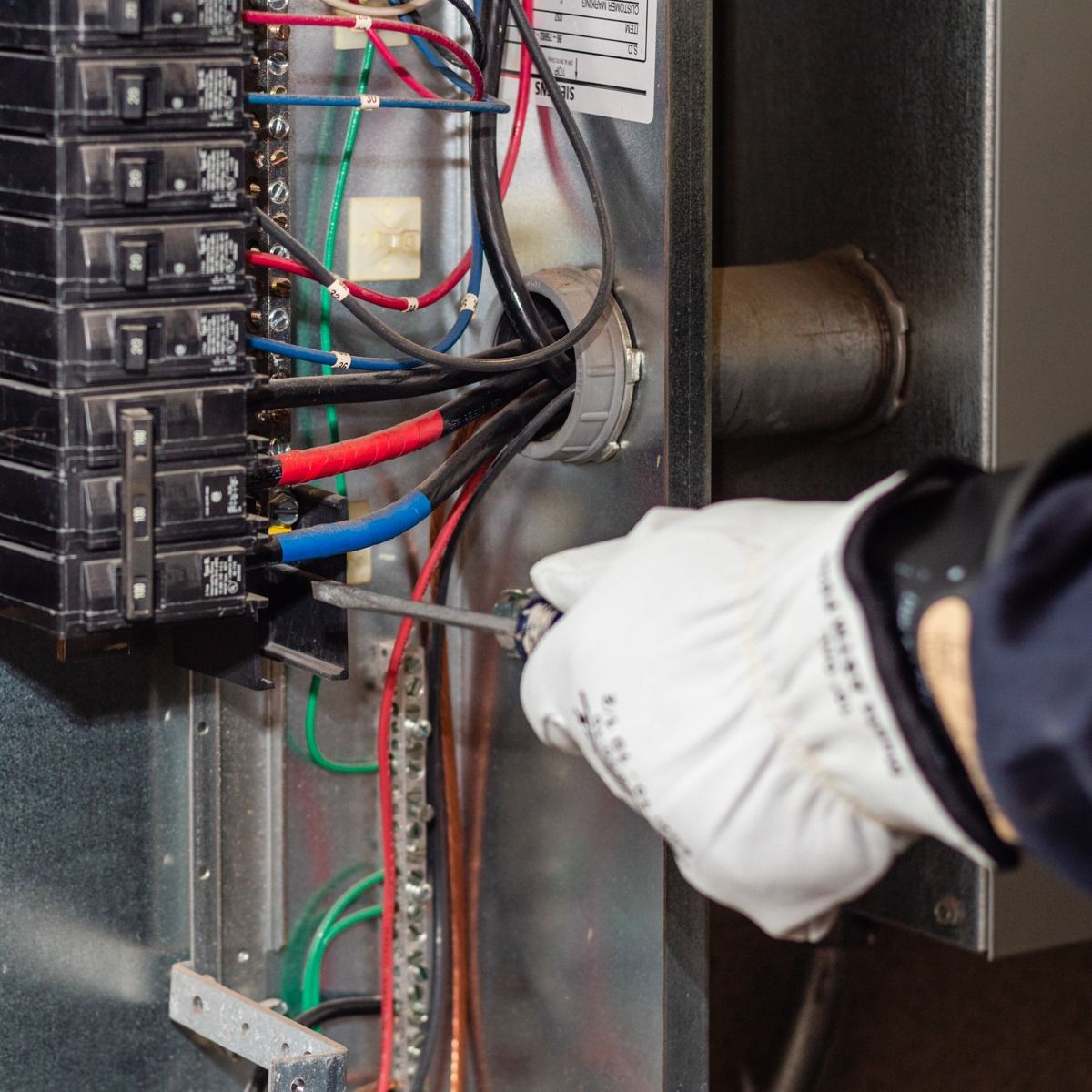 Electrician tightening wires in electrical panel with a screwdriver, wearing protective gloves.