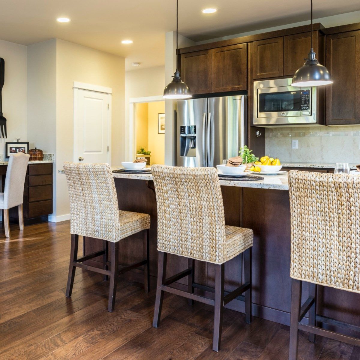 Kitchen with island and wicker barstools, dark wood cabinets, stainless steel appliances, and hardwood floors.