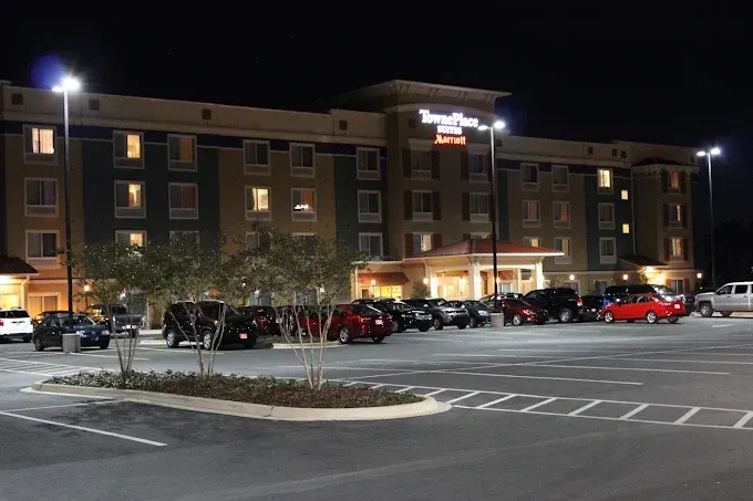 Hotel exterior at night with lit parking lot and cars.