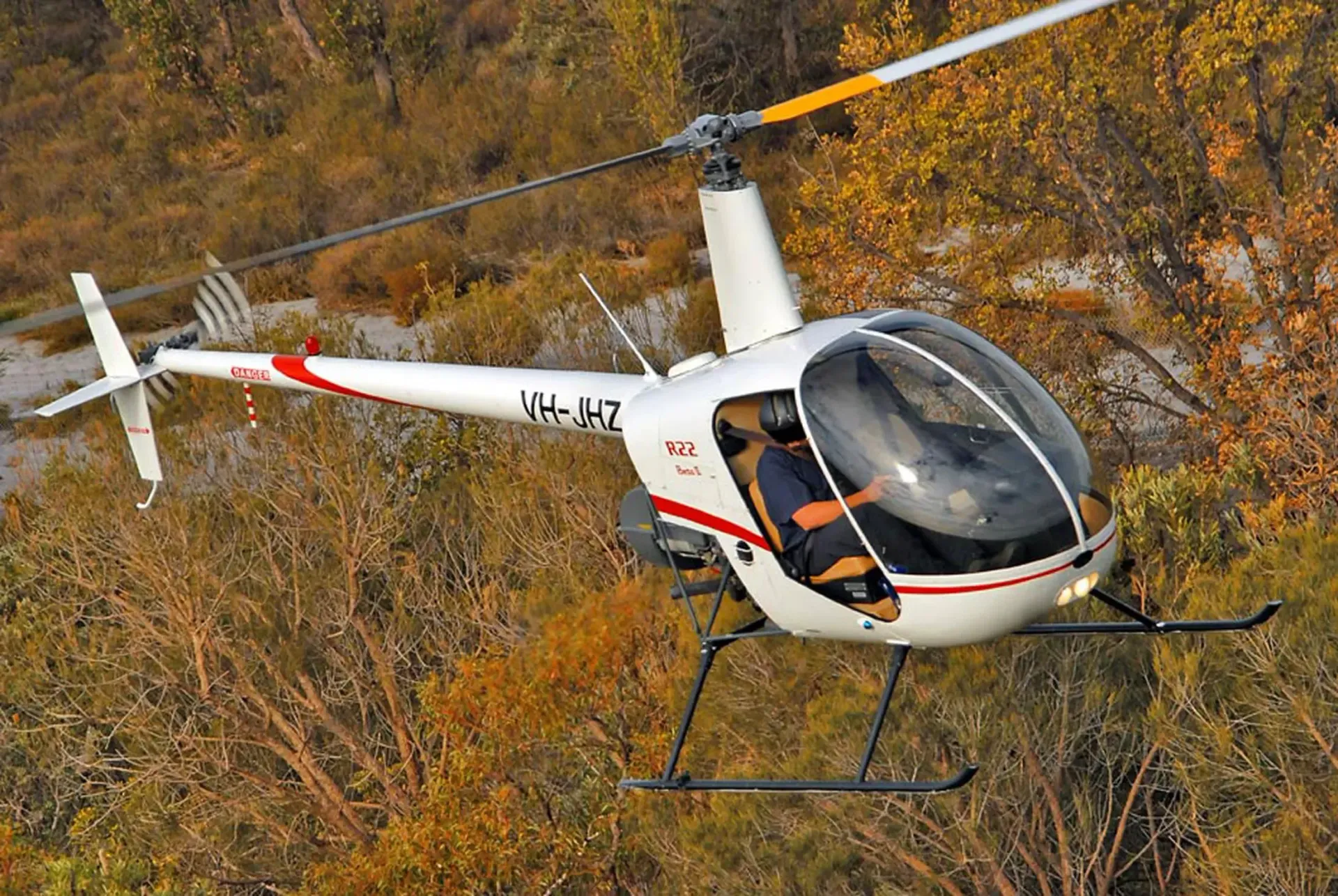 A small white helicopter is flying over a forest