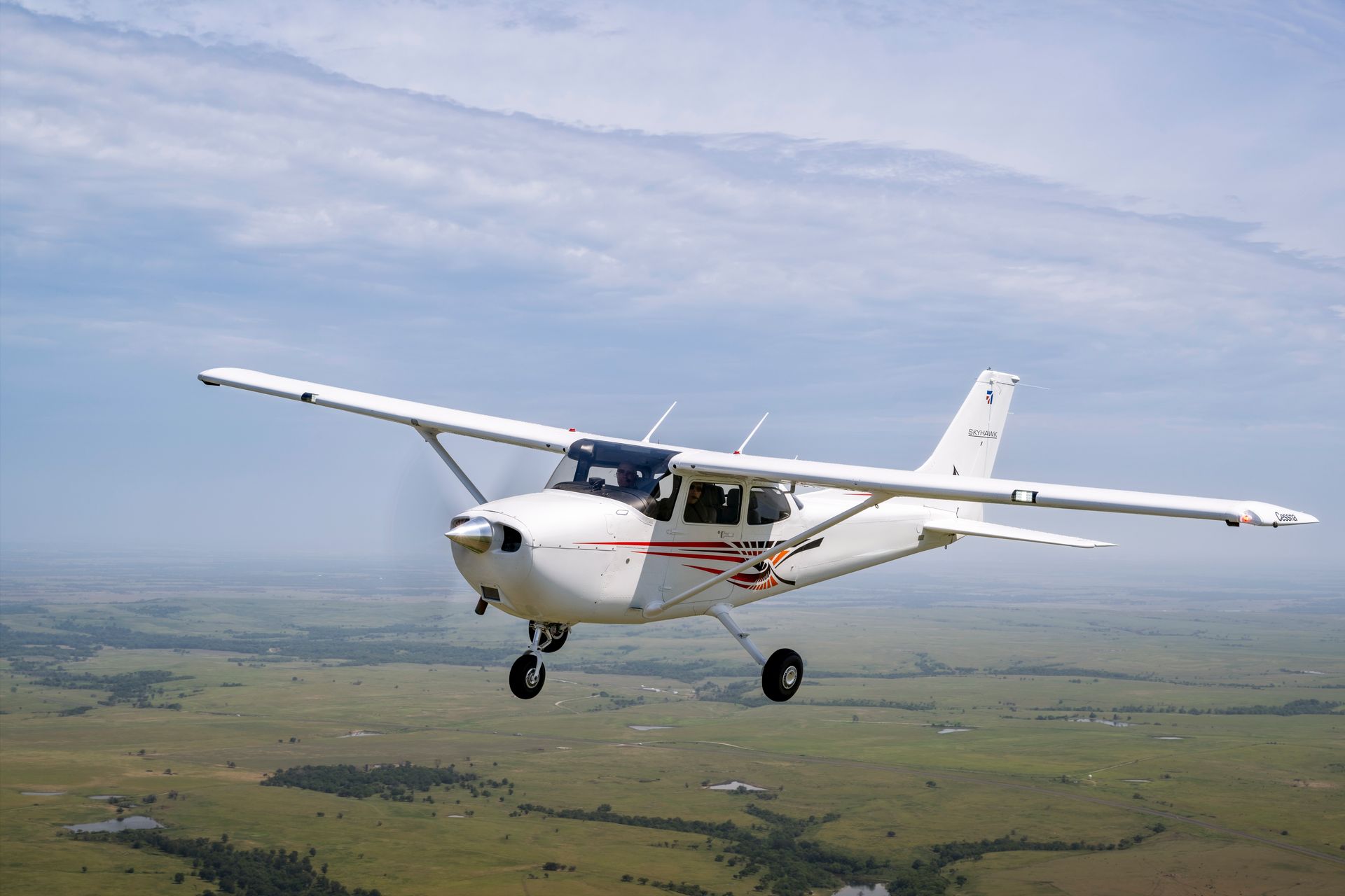 A small plane is flying over a grassy field.
