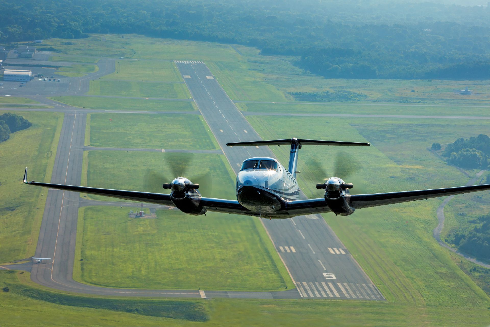 A small propeller plane is flying over an airport runway.