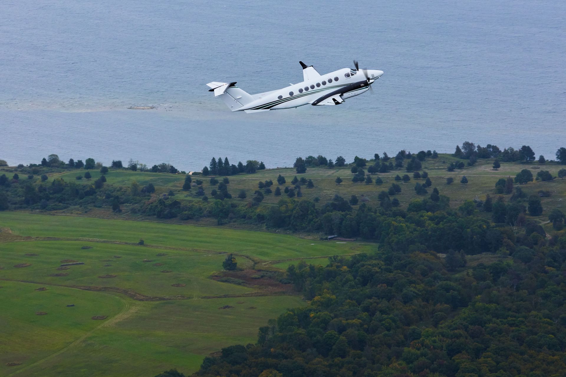 A small propeller plane is flying over an airport runway.