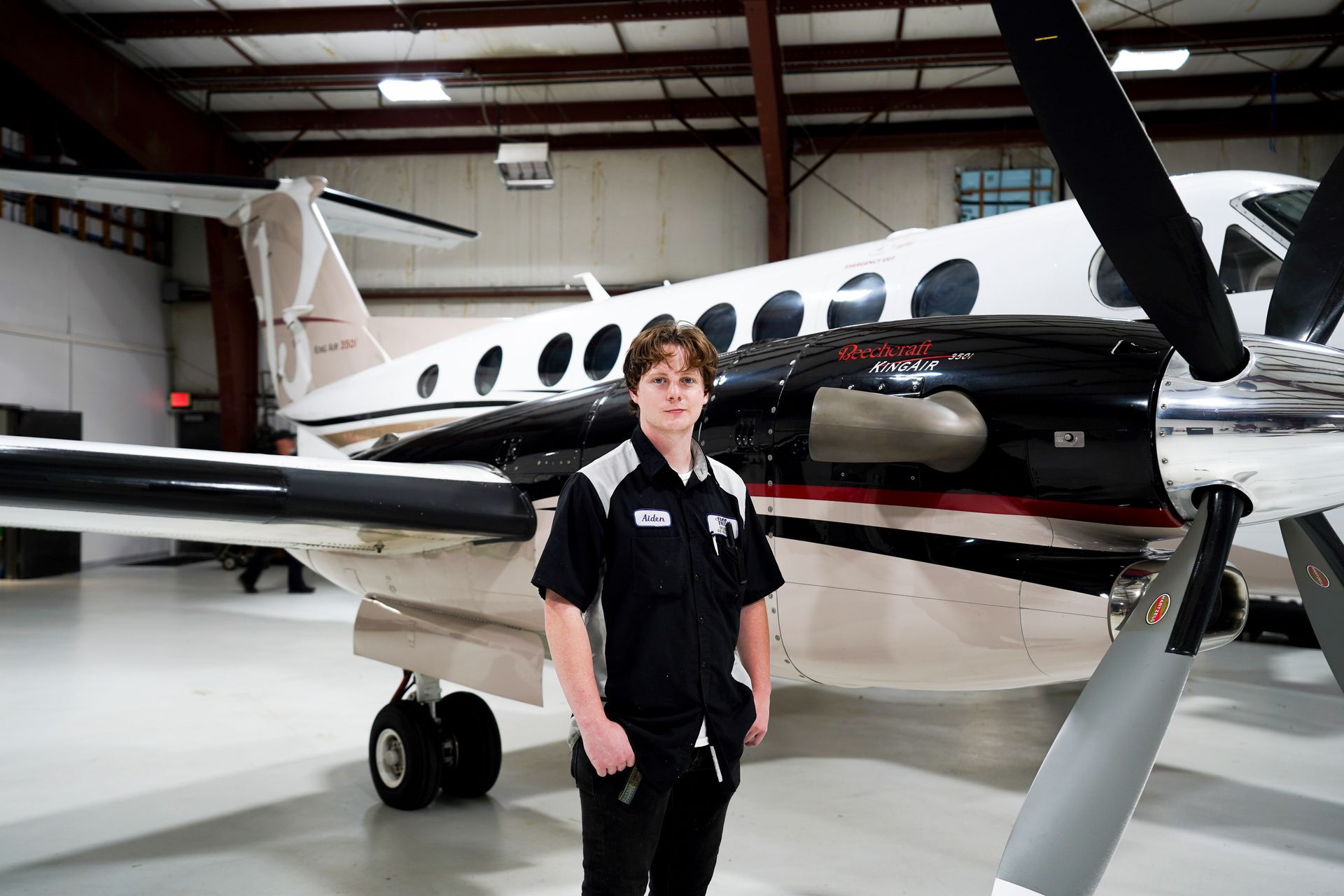 A young man is standing in front of an airplane in a hangar.