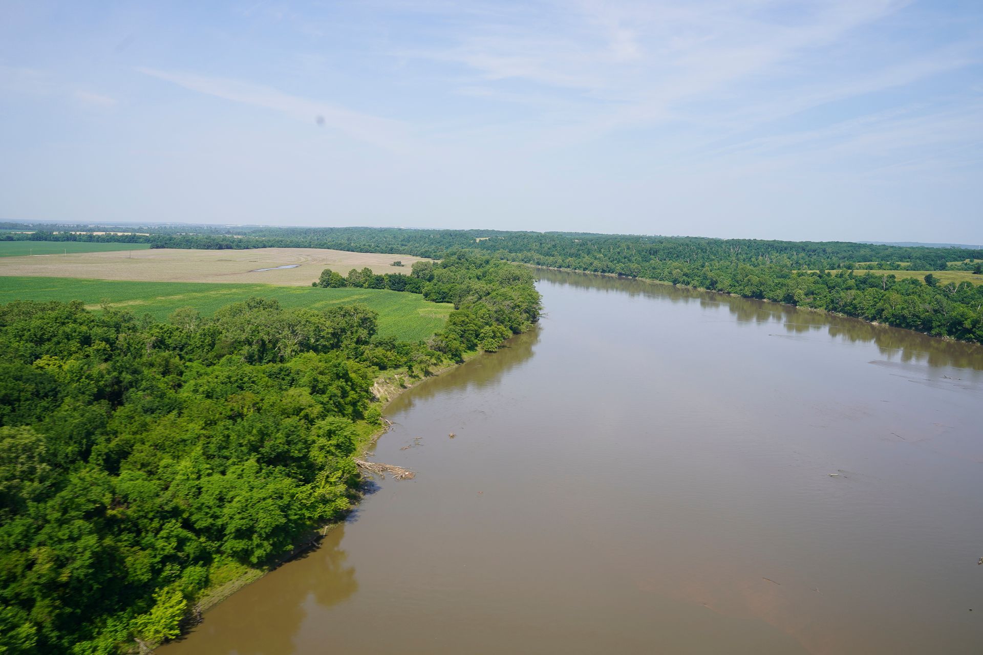 An aerial view of a river surrounded by trees and fields on a sunny day.