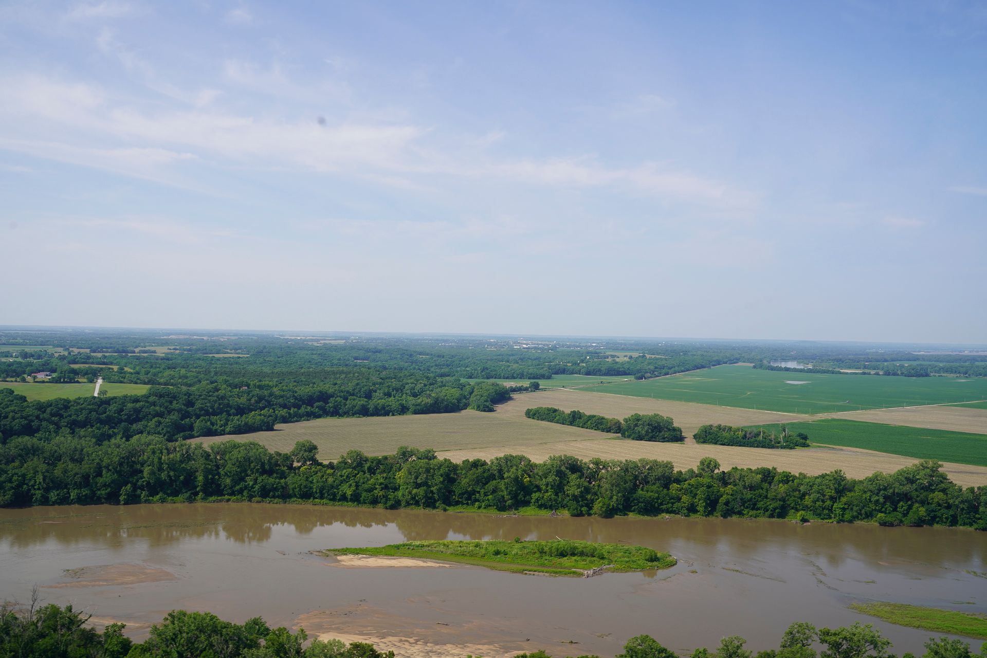An aerial view of a river surrounded by trees and fields on a sunny day.