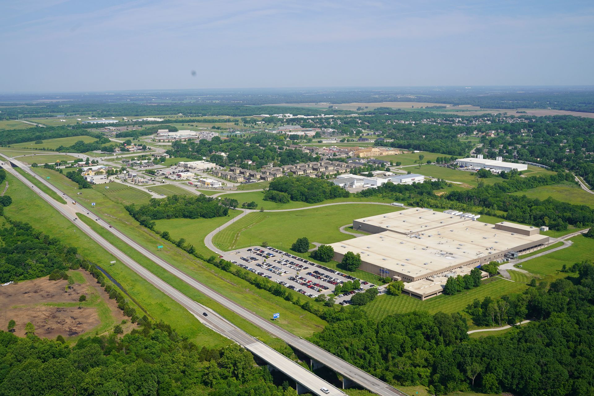 An aerial view of a large industrial area surrounded by trees and a highway.