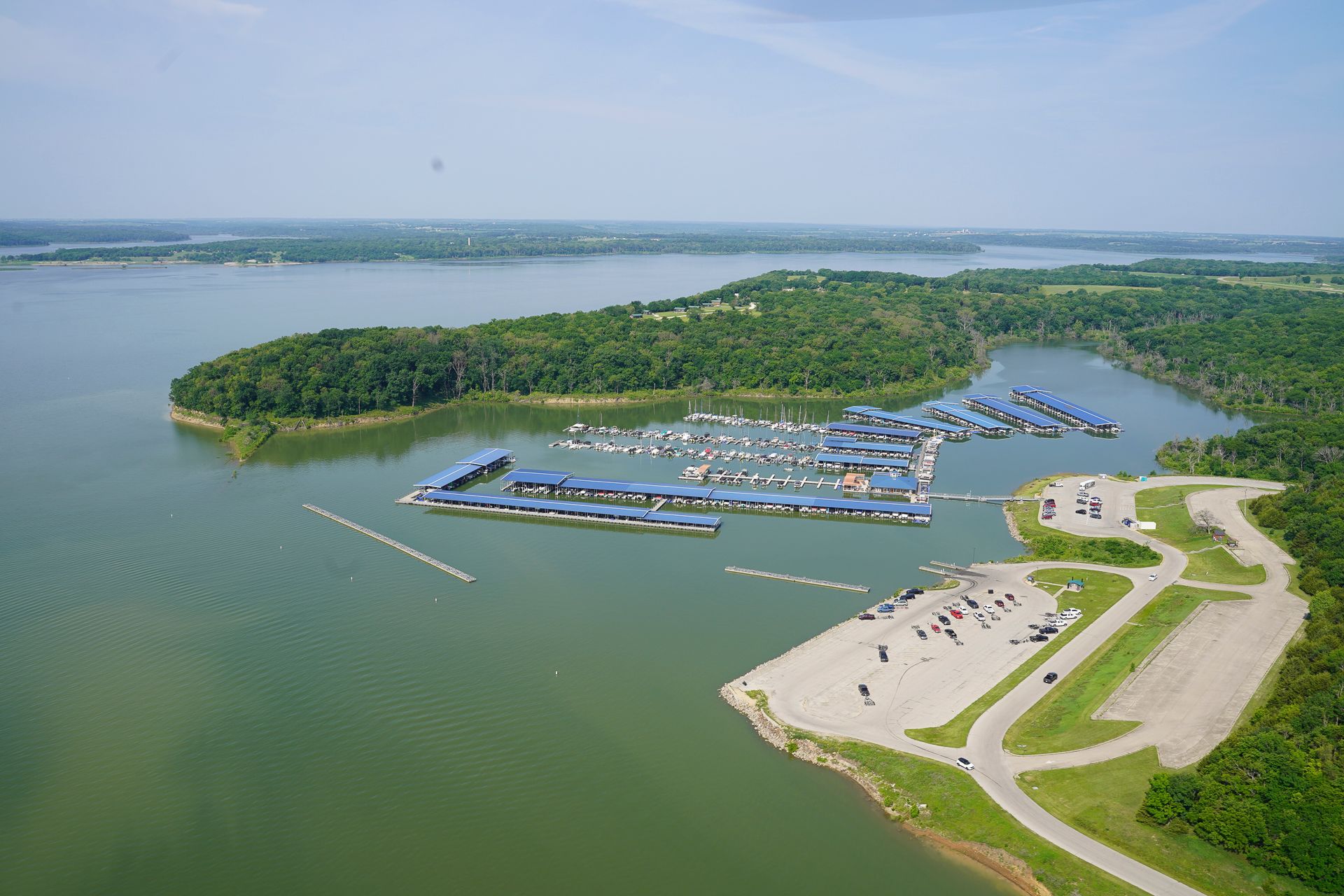 An aerial view of a marina on a large body of water surrounded by trees.