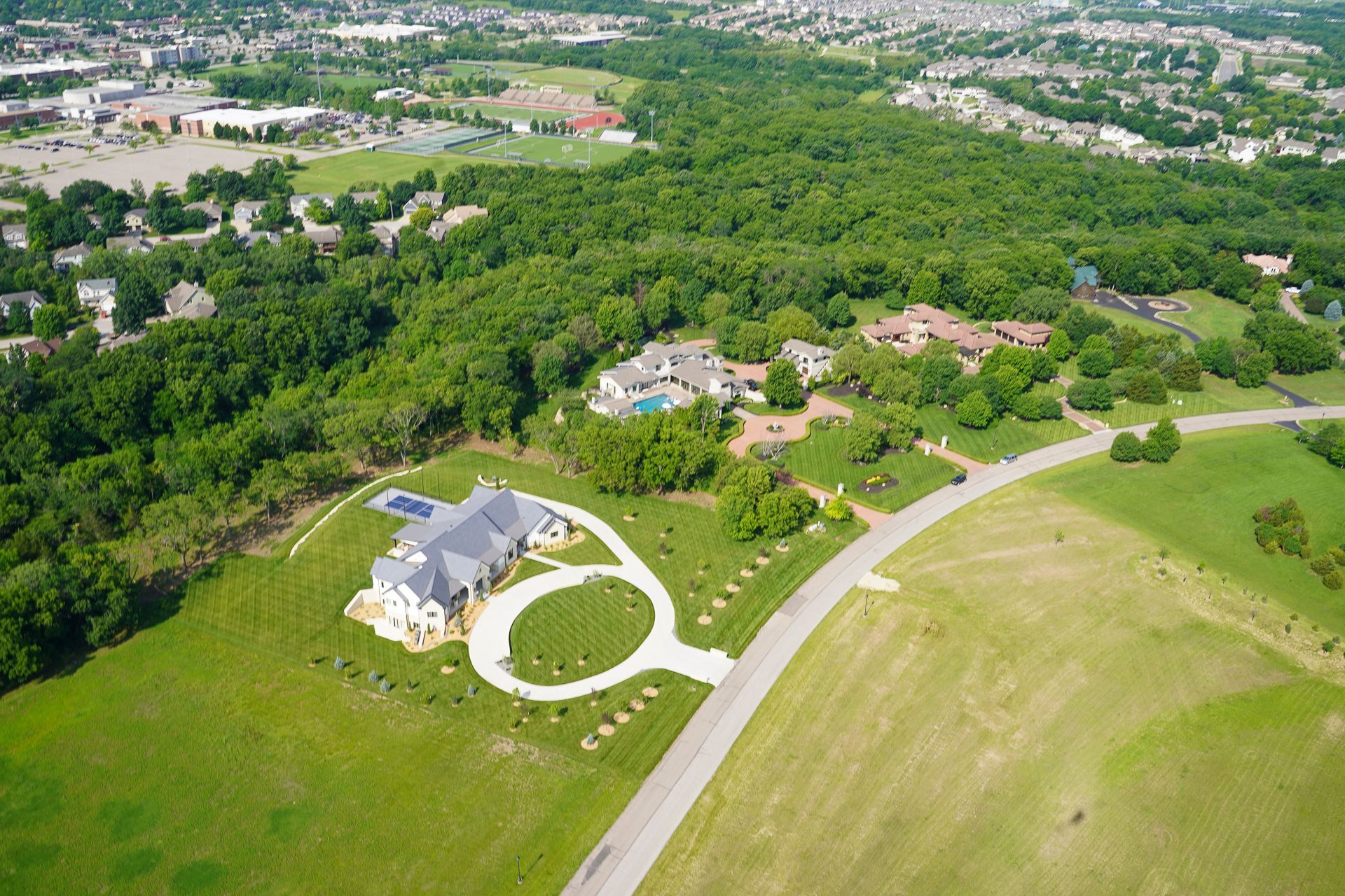 An aerial view of a house in the middle of a lush green field surrounded by trees.