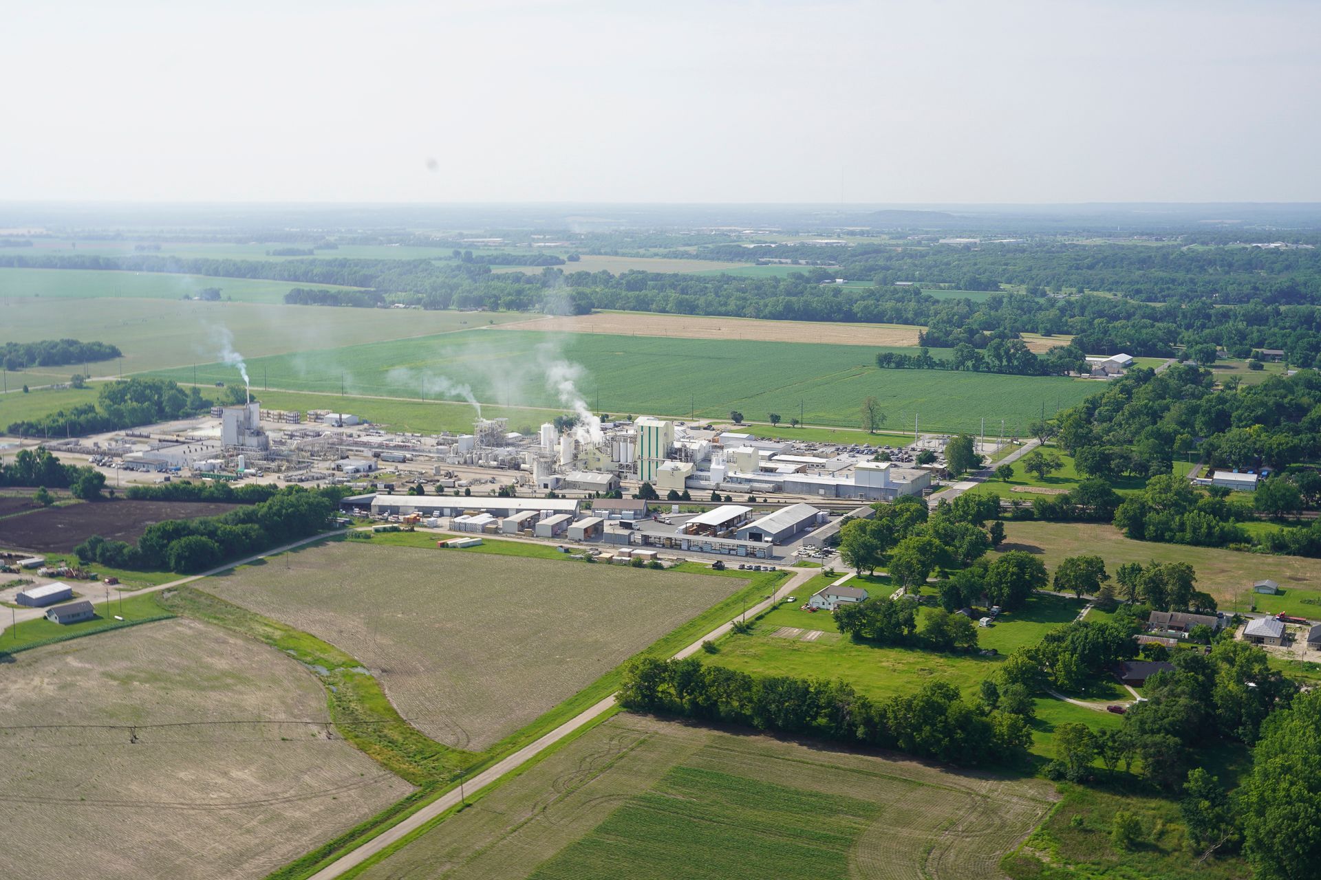 An aerial view of a factory surrounded by fields and trees.