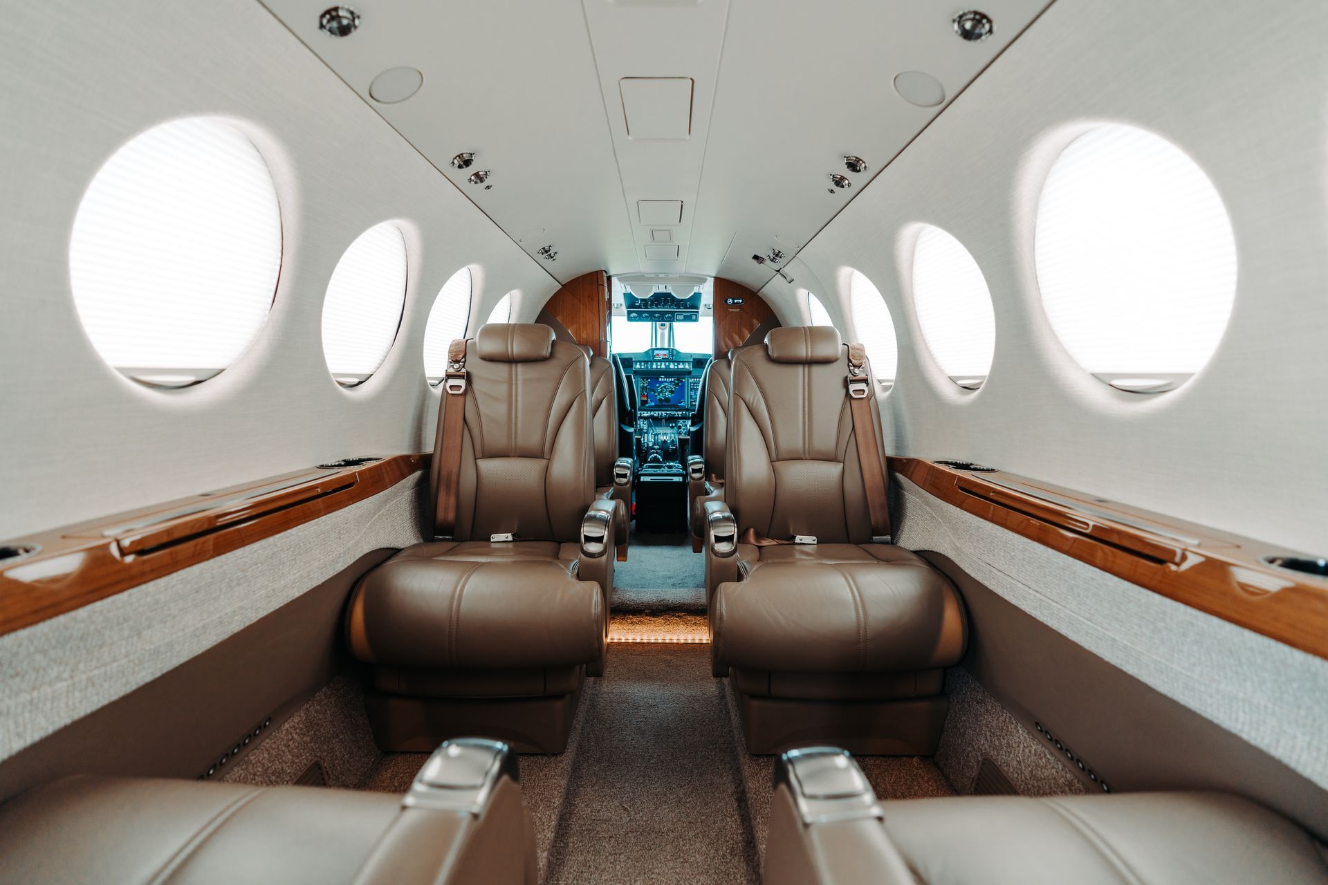 The inside of a private jet with brown leather seats and a cockpit.