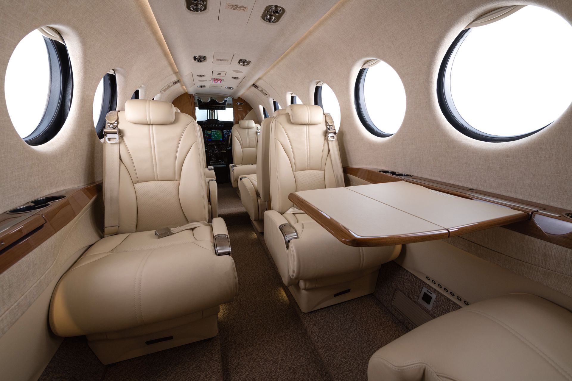 The inside of a private jet with brown leather seats and a cockpit.