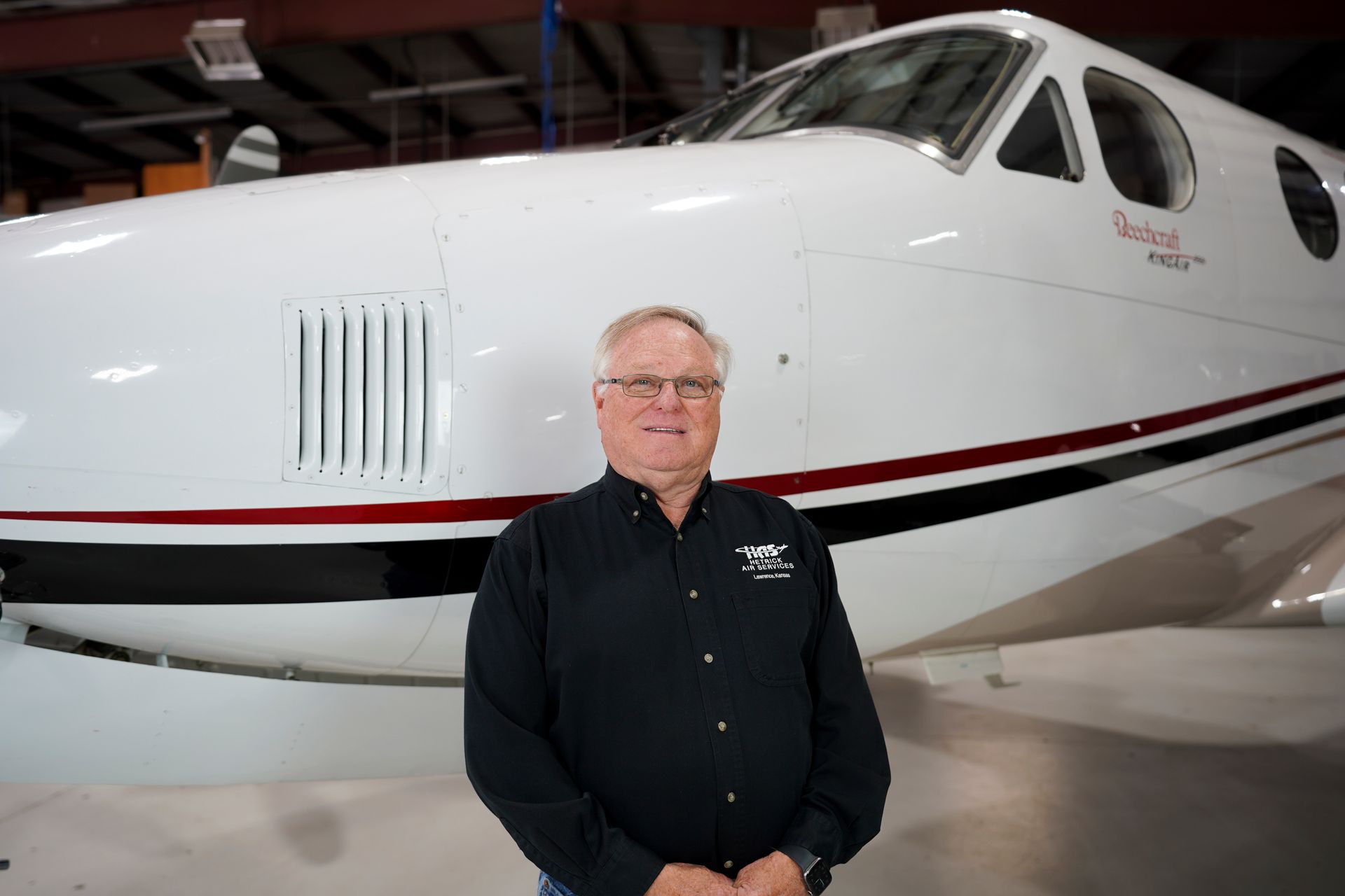 A man in a black shirt is standing in front of an airplane.