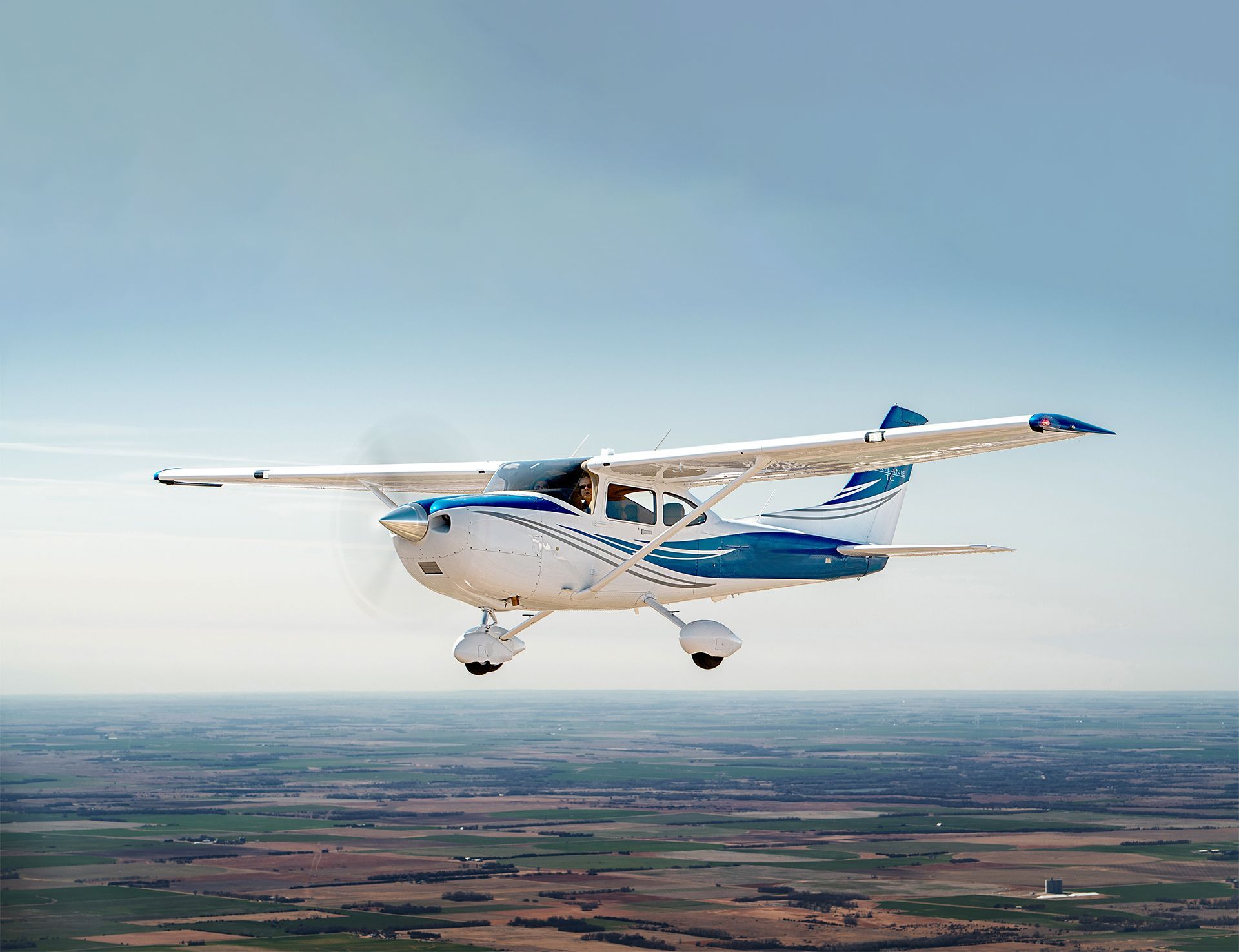 A small plane is flying over a lush green field.