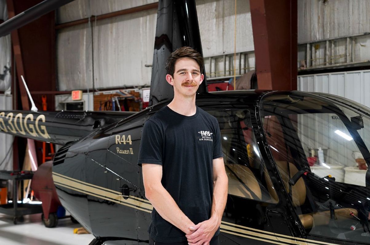 A man is standing in front of a black helicopter in a hangar.