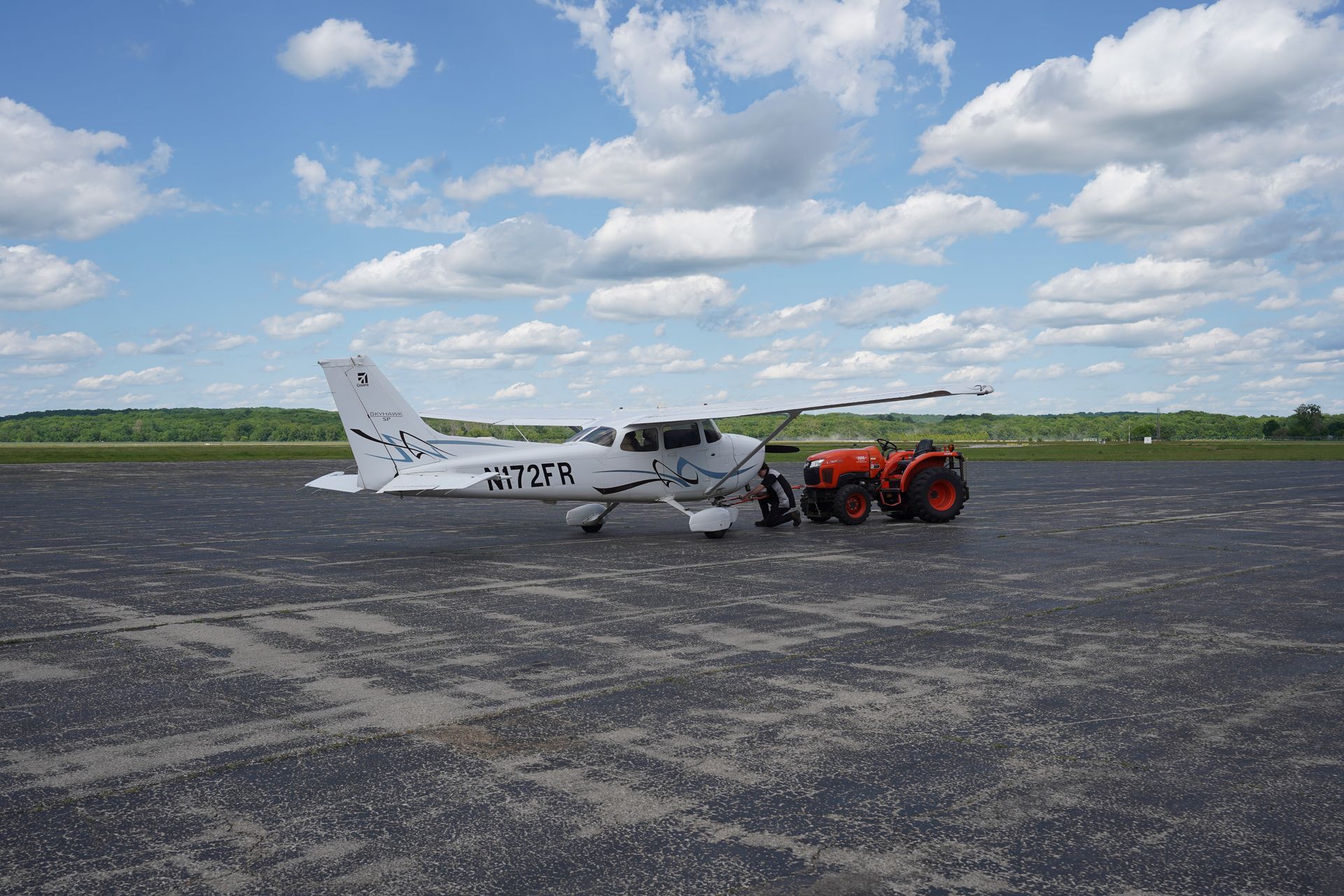 A small plane is parked next to a tractor on a runway.
