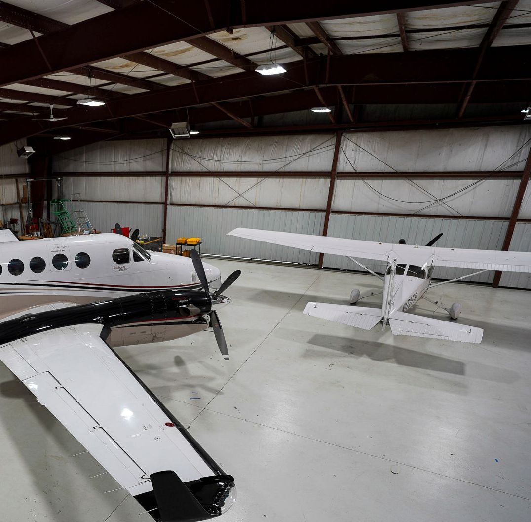 A plane is parked in a hangar with another plane in the background.