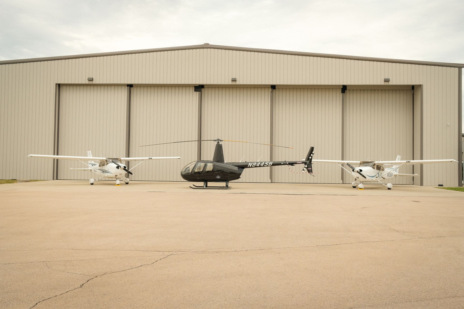 Three small planes are parked in front of a hangar.