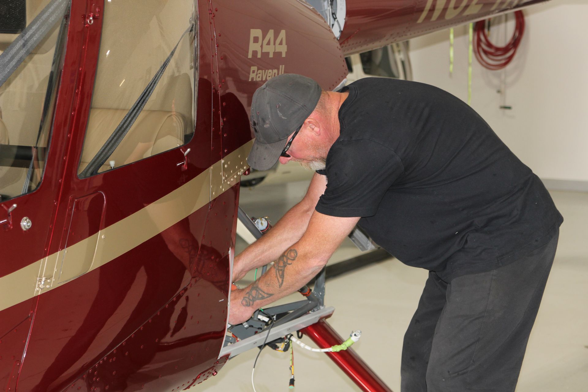 A man is working on a red helicopter in a hangar.