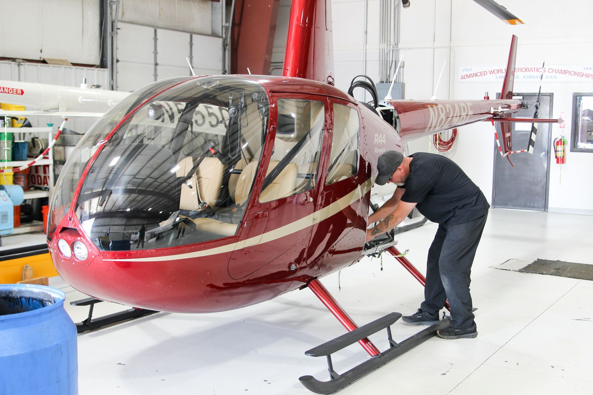 A man is working on a red helicopter in a hangar.