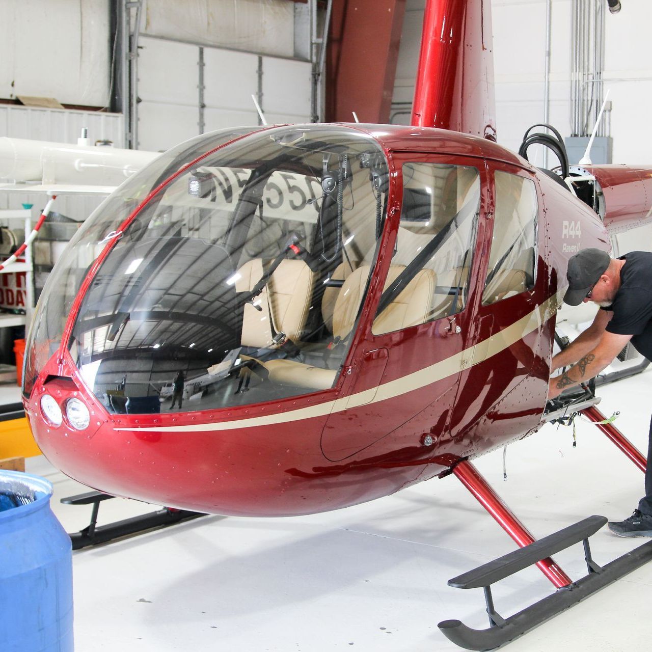 A man is working on a red helicopter in a hangar.