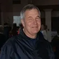 A man in a black jacket is smiling for the camera in a dark room.