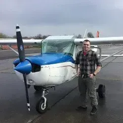 A man is standing in front of a small plane on a runway.