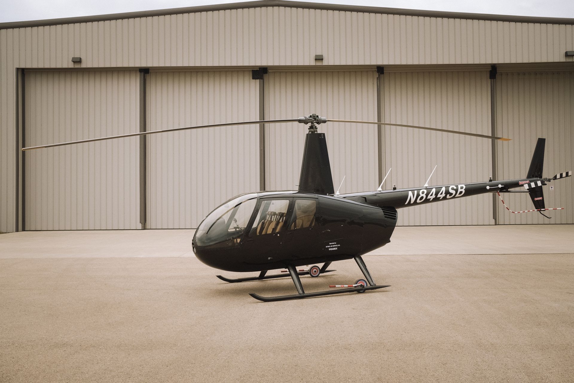 A black helicopter is parked in front of a hangar.