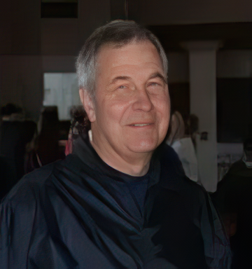 A man in a black jacket is smiling for the camera in a dark room.