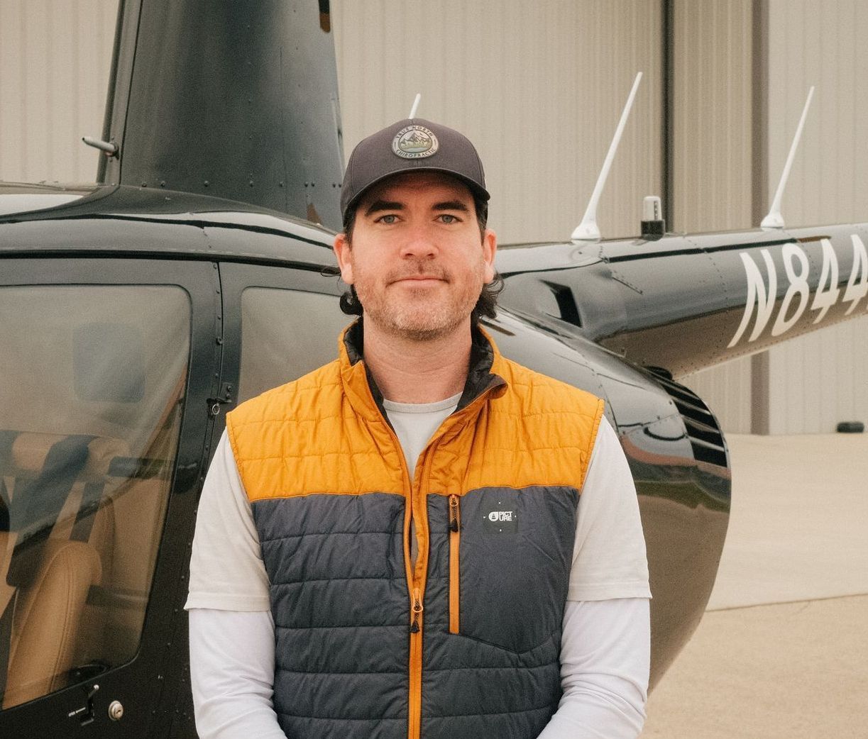 A man is standing in front of a black helicopter in a hangar.