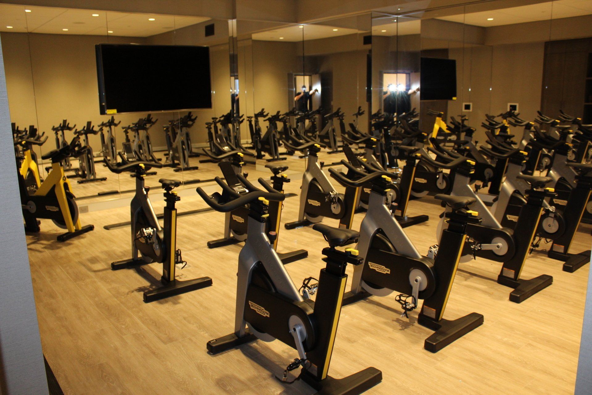 Spacious spin studio with mirrored wall and multiple stationary bikes.