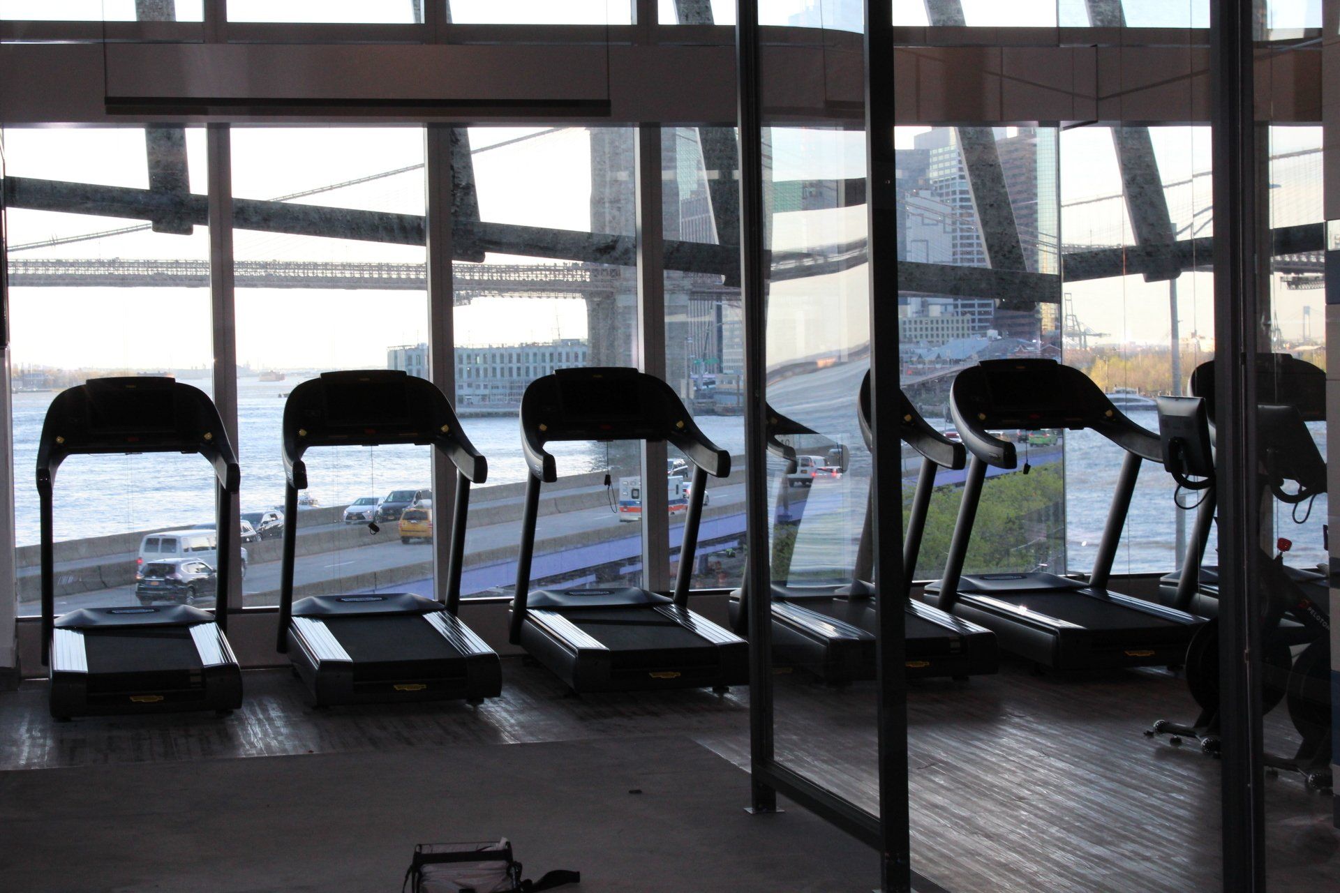 Row of treadmills by floor-to-ceiling windows with bridge and city views at One Manhattan Square.