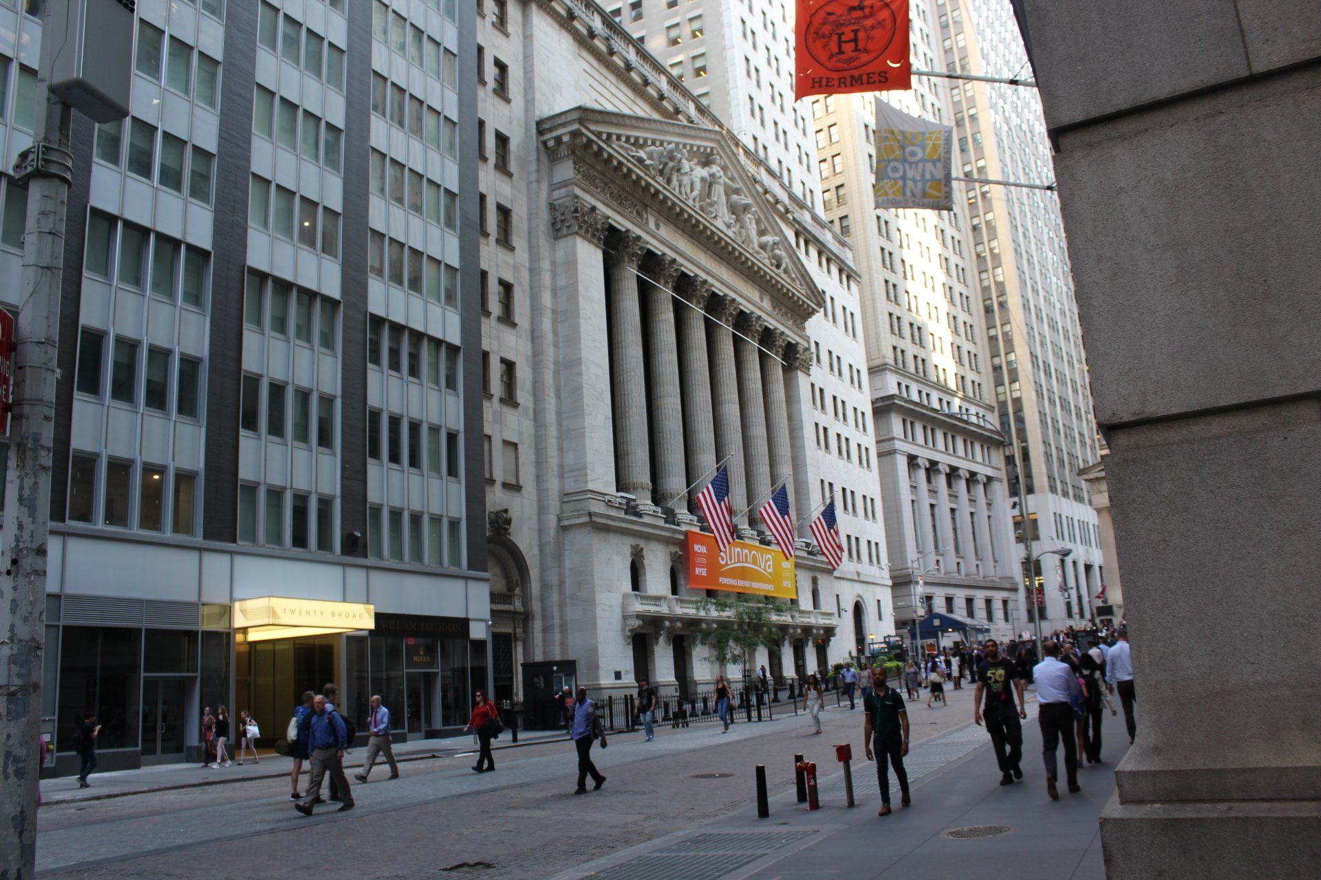Street view of Wall Street near Twenty Exchange Place with pedestrians and buildings.
