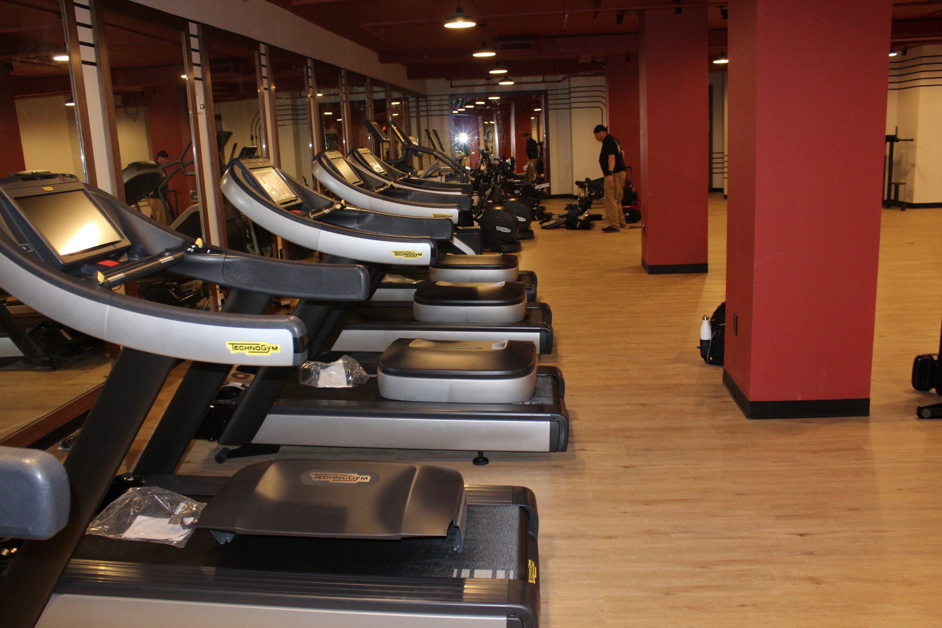Row of treadmills inside a modern fitness center with wood flooring and red accent walls